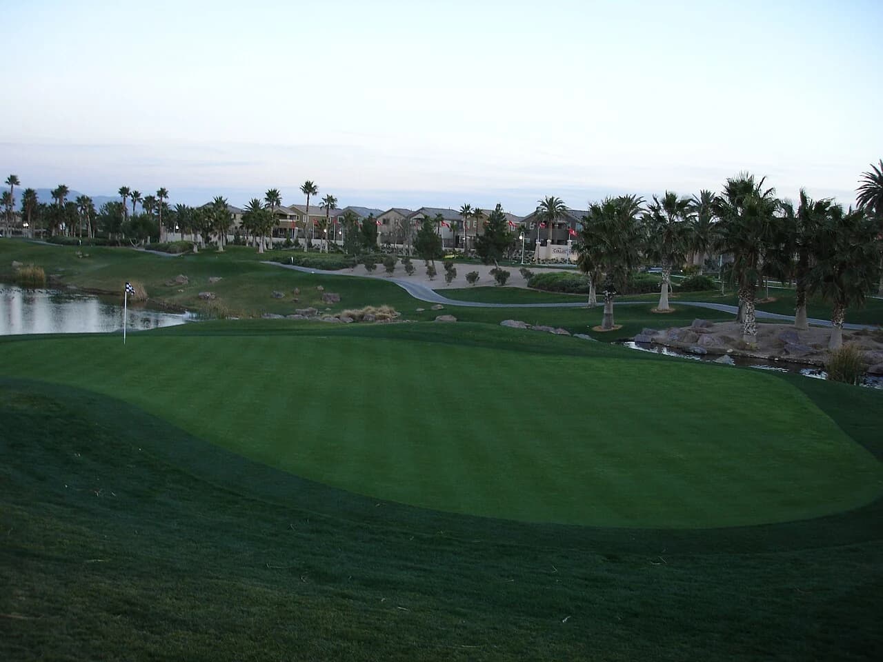 Rhodes Ranch golf course with a putting green, water, palm trees and clubhouse beyond